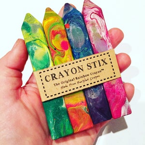 May include: A set of four colorful crayon stix, made from recycled crayons. The crayons are in a hand, and the label reads "Crayon Stix, The Original Rainbow Crayon, Made from Recycled Crayons."