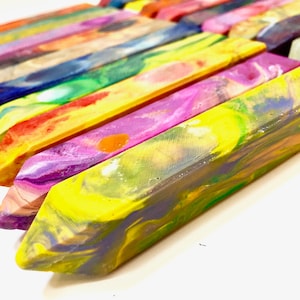 May include: A close-up of a set of colorful, swirled crayons. The crayons are arranged in a row, with the tips of the crayons pointing towards the right side of the image. The crayons are a variety of colors, including yellow, green, blue, purple, and red.