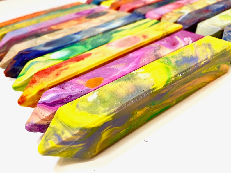 May include: A close-up of a set of colorful, swirled crayons. The crayons are arranged in a row, with the tips of the crayons pointing towards the right side of the image. The crayons are a variety of colors, including yellow, green, blue, purple, and red.