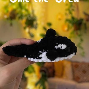 May include: A crocheted black and white orca, named Ollie, with the text "Ollie the Orca Crochet Pattern No-sew!"