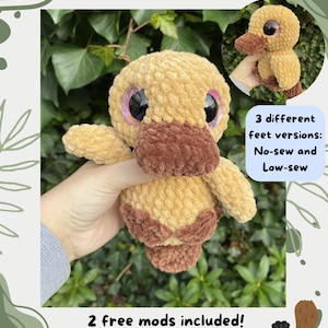 Op de afbeelding: Een gehaakte platypus knuffel in tinten van bruin en beige, met grote, glinsterende roze en zwarte ogen. De afbeelding bevat de tekst "Phoebe the Platypus" en "Crochet pattern by @joolscrochetplushies."