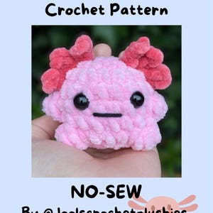Könnte beinhalten: Ein rosa gehäkeltes Axolotl-Plüschtier mit roten Kiemen und schwarzen Augen. Das Bild enthält den Text "Alice the Axolotl Crochet Pattern" und "NO-SEW" sowie den Handle des Erstellers. Das Plüschtier wird in einer Hand gehalten.