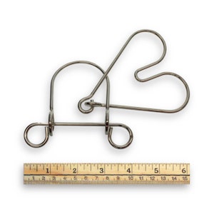 May include: A silver metal puzzle in the shape of a heart. The puzzle is made of four pieces of wire that are bent and intertwined. A ruler is shown below the puzzle for scale.
