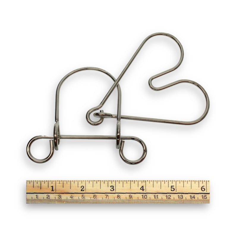 May include: A silver metal puzzle in the shape of a heart. The puzzle is made of four pieces of wire that are bent and intertwined. A ruler is shown below the puzzle for scale.