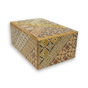 Peut inclure: Une boîte en bois avec un motif géométrique composé de bois de différentes couleurs. La boîte est fermée et a une forme rectangulaire.
