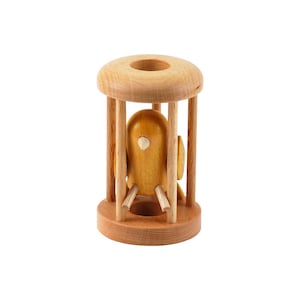May include: A light brown wooden birdcage toy featuring a smooth, cylindrical frame with vertical bars. Inside the cage sits a small, yellow wooden bird figure with a white beak, positioned on a central perch within the structure.