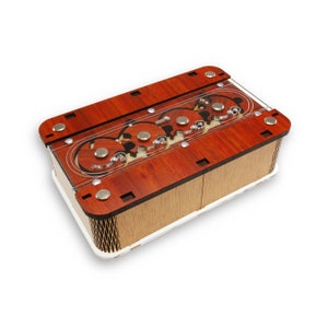 May include: A wooden box with a clear plastic top, revealing a series of interlocking gears. The box is made of light and dark wood, with a reddish-brown stain. The gears are made of metal and are visible through the clear plastic top.