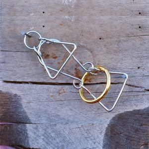 May include: A metal puzzle with a silver frame and a gold-coloured ring. The puzzle features geometric shapes, including triangles and a circle, interlocked. The puzzle is designed to challenge problem-solving skills.