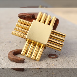 May include: A gold metal puzzle with a square centre and eight rods extending out from the centre. The puzzle is lying on a light brown surface.