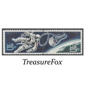 Puede incluir: Un sello postal estadounidense vintage que presenta una ilustración en blanco y negro de un astronauta con un traje espacial flotando en el espacio con una pequeña nave espacial. El sello es azul con un borde verde y el texto "US 5c" en rojo.