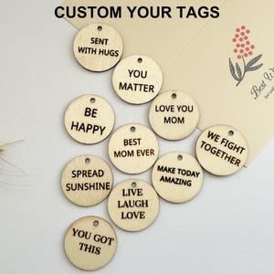 May include: A set of 11 round wooden tags with various inspirational messages, such as "You Matter", "Be Happy", "Spread Sunshine", and "Live Laugh Love".