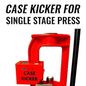 Pode incluir: Um "Case Kicker" vermelho para uma prensa de estágio único, com o texto "CASE KICKER FOR SINGLE STAGE PRESS" em preto. Um estojo de cartucho de latão é ejetado do dispositivo. O dispositivo foi projetado para recarregar munição.