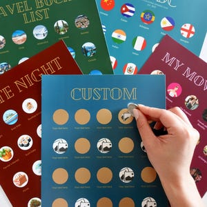 May include: A selection of scratch-off cards with themes like travel, date nights, and custom options. The cards feature gold foil details and are in colours of green, burgundy, and blue. A hand is shown scratching off a circle on a blue custom card.