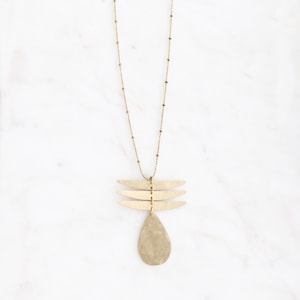 May include: A gold necklace with a delicate chain and a pendant featuring three horizontal bars and a teardrop shape.