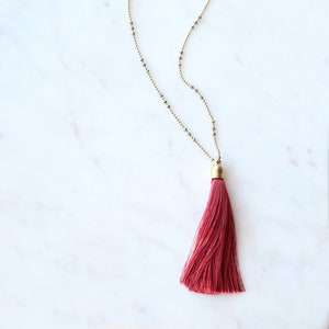 May include: A gold chain necklace with a long, burgundy tassel pendant.