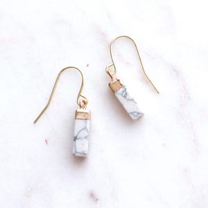 May include: A pair of gold dangle earrings with white marble rectangular stones. The stones have a gold trim around the top.