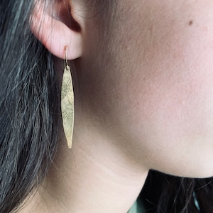May include: Gold dangle earrings with a textured, elongated oval shape.