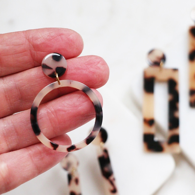 May include: A pair of statement earrings with a tortoiseshell pattern. One earring features a large circle and the other a rectangle.