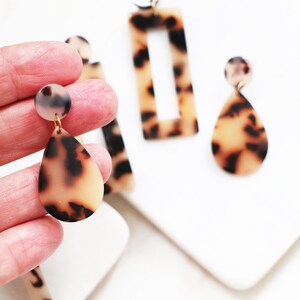 May include: A pair of tortoise shell earrings with gold posts. One earring is a teardrop shape and the other is a rectangle with a cutout.