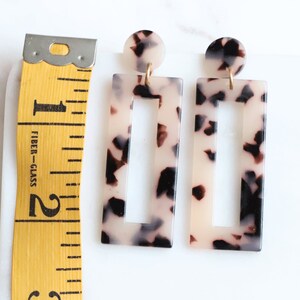 May include: A pair of rectangular tortoiseshell earrings with a gold accent. The earrings have a cutout design in the center.