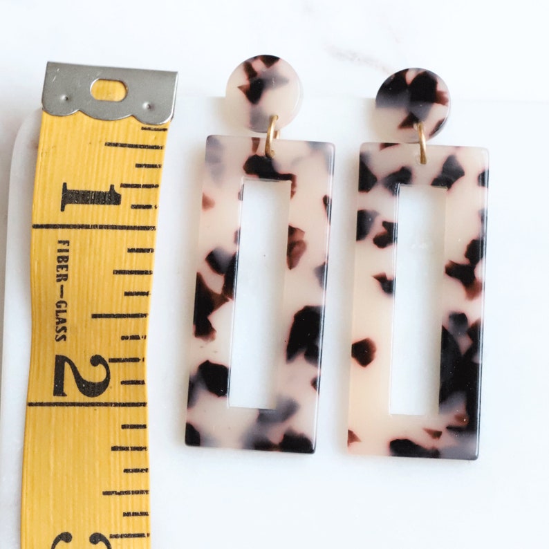 May include: A pair of rectangular tortoiseshell earrings with a gold accent. The earrings have a cutout design in the center.