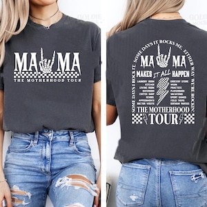 May include: Dark gray t-shirt with the text "MAMA" in white, featuring a skeleton hand gesture. The front reads "THE MOTHERHOOD TOUR." The back of the shirt says "MAMA MAKES IT ALL HAPPEN" with a list of activities.