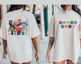 Könnte beinhalten: Zwei Frauen tragen elfenbeinfarbene T-Shirts mit einem grafischen Druck von Figuren aus dem Film Inside Out. Die Vorderseite des Shirts zeigt eine Reihe von kreisförmigen Symbolen mit verschiedenen Gesichtsausdrücken. Die Rückseite des Shirts zeigt eine Gruppe von Figuren mit verschiedenen Emotionen.