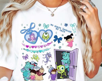 May include: White t-shirt featuring a colorful graphic of characters from the animated film Monsters, Inc. The design includes Mike Wazowski, Sulley, Boo, and the text "we scare because we care". The graphic is surrounded by bows and hearts.