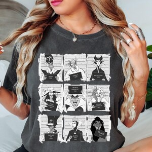 Puede incluir: Camiseta gris oscuro con una cuadr&iacute;cula de im&aacute;genes en blanco y negro de villanos de Disney al estilo de fotos policiales. Cada imagen incluye el nombre del personaje y un n&uacute;mero. La camiseta es de estilo casual y c&oacute;modo.