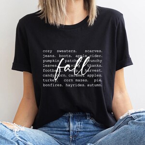 Może przedstawiać: Czarny T-shirt z białym tekstem, kt&oacute;ry brzmi "cozy sweaters. scarves. jeans. boots. apple cider. pumpkin patch. crunchy leaves. fall. thanks. football. soup. harvest. candy corn. caramel apples. turkey. corn mazes. pie. bonfires. hayrides. autumn."