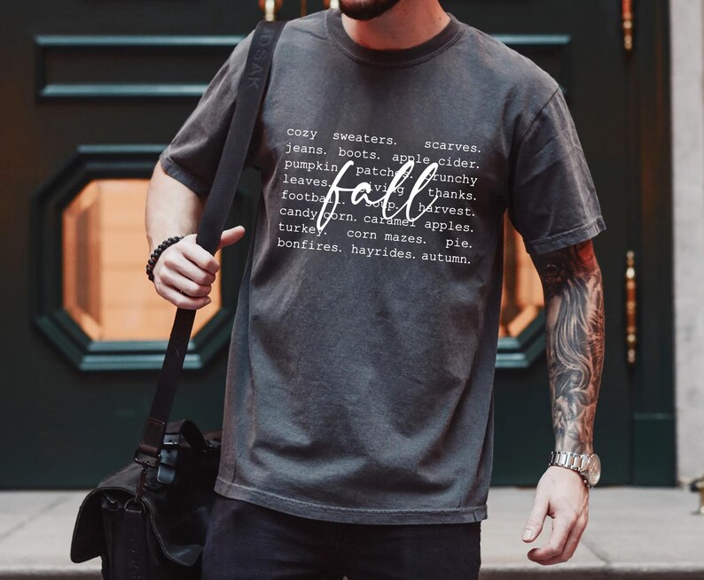 Może przedstawiać: Szary T-shirt z białym nadrukiem graficznym, na kt&oacute;rym widnieje napis "przytulne swetry, szaliki, dżinsy, buty, cydr jabłkowy, pole dyni, liście, jesień, chrupiący, dzięki, piłka nożna, zbiory, cukrowe kukurydza, jabłka karmelowe, indyk, labirynty kukurydziane, ciasto, ogniska, przejażdżki bryczką, jesień."