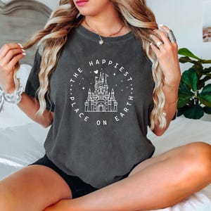 May include: A dark gray t-shirt with a white graphic of Cinderella's castle and the text "The Happiest Place on Earth".