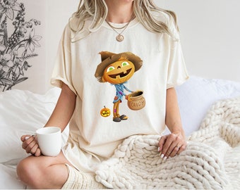 May include: A cream coloured t-shirt featuring a cartoon pumpkin scarecrow holding a bag that says "CANDY".
