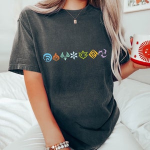May include: Dark grey t-shirt with a series of colourful symbols across the chest. The symbols are in blue, orange, green, white, yellow, and purple. The t-shirt has short sleeves and a relaxed fit.
