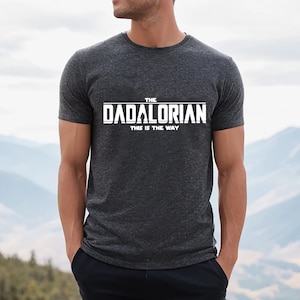 May include: A dark gray t-shirt with white text that reads "The Dadalorian This is the Way".