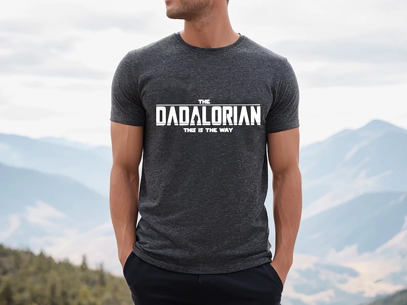 May include: A dark gray t-shirt with white text that reads "The Dadalorian This is the Way".