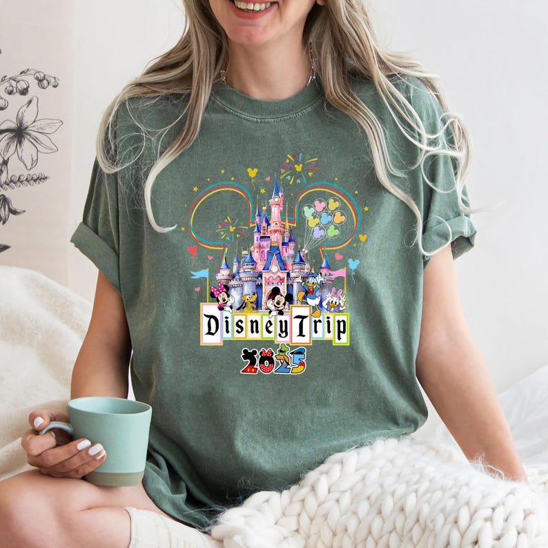 May include: Green t-shirt with a graphic of Cinderella's castle, Mickey Mouse, Minnie Mouse, Donald Duck, Goofy, and Pluto. The text "Disney Trip 2023" is printed below the graphic.