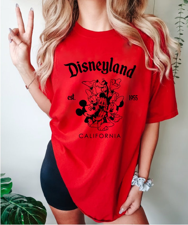 May include: Red t-shirt with a black graphic of Mickey Mouse and friends. The graphic includes the text "Disneyland est. 1955 California".