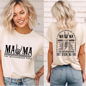 May include: Cream-colored t-shirt with the text "MAMA" in a bold, black font, featuring a skeleton hand gesture. The shirt also includes "THE MOTHERHOOD TOUR" and a checkered pattern. The back of the shirt has additional text and graphics.