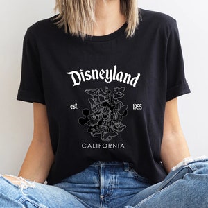 May include: Black t-shirt with a white graphic of Mickey Mouse and other Disney characters. The text "Disneyland est. 1955 California" is printed on the shirt.