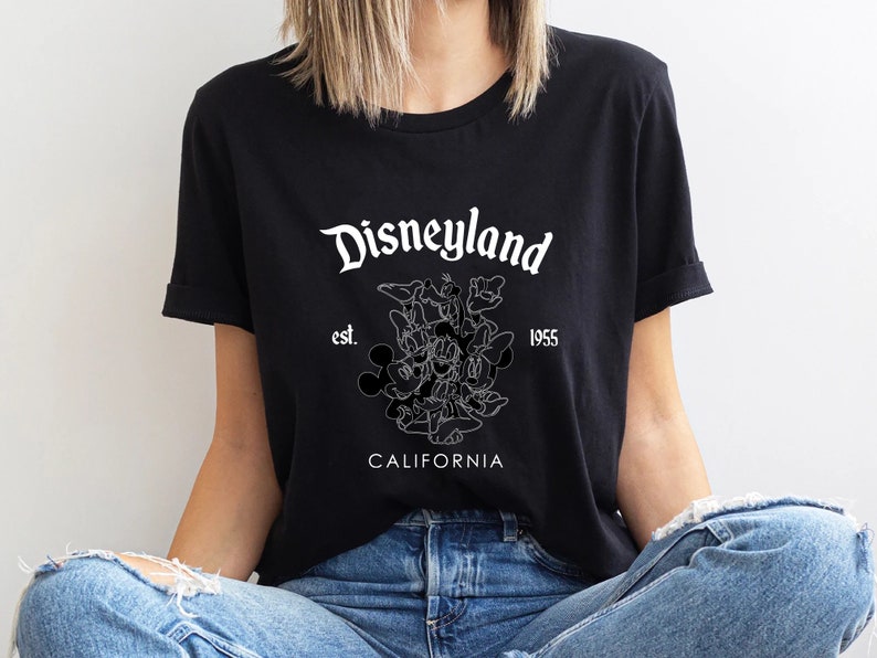 May include: Black t-shirt with a white graphic of Mickey Mouse and other Disney characters. The text "Disneyland est. 1955 California" is printed on the shirt.
