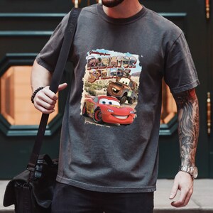 May include: A gray t-shirt with a graphic print of Lightning McQueen and Mater from the movie Cars. The graphic says "Greetings from Radiator Springs".
