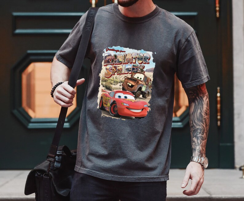 May include: A gray t-shirt with a graphic print of Lightning McQueen and Mater from the movie Cars. The graphic says "Greetings from Radiator Springs".