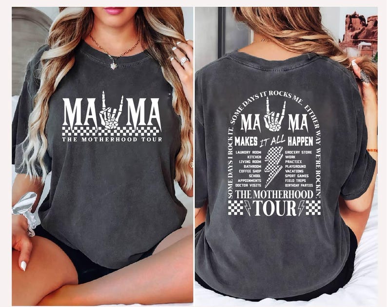 May include: Dark gray t-shirt with the text "MAMA" in white, featuring a skeleton hand gesture. The shirt also includes "THE MOTHERHOOD TOUR" and a list of activities. The back of the shirt has the text "MA MA MAKES IT ALL HAPPEN".