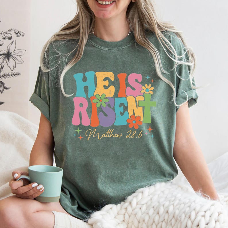May include: A green t-shirt with a retro-style graphic that says "He is Risen" with flowers and stars. The text "Matthew 28:6" is below the graphic.
