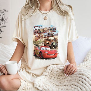 May include: A white t-shirt with a graphic print of Lightning McQueen and Mater from the movie Cars. The graphic says "Greetings from Radiator Springs".