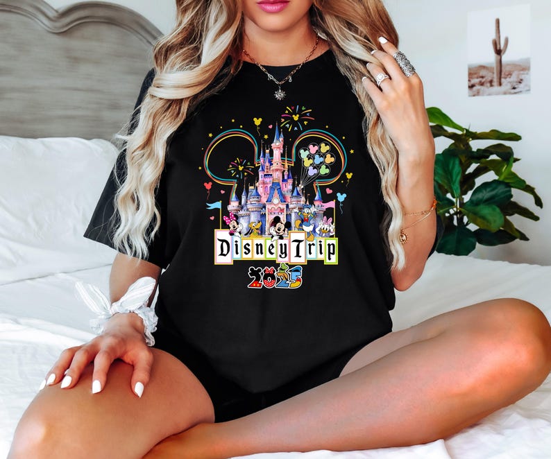 May include: Black t-shirt with a colorful graphic of Cinderella's castle and Disney characters. The text "Disney Trip 2023" is printed below the graphic.