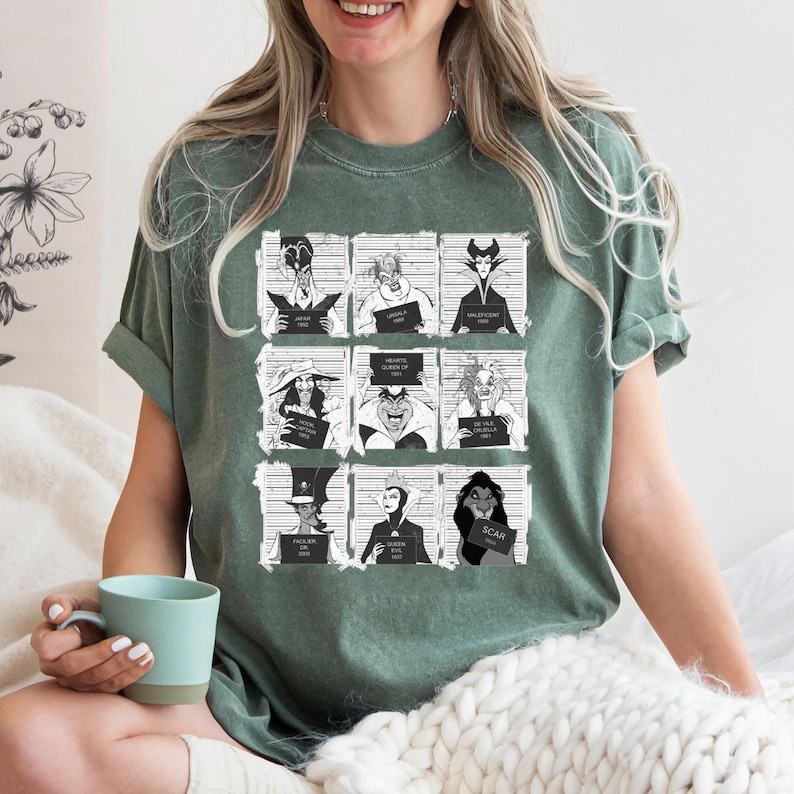 Puede incluir: Camiseta verde con una cuadr&iacute;cula de nueve villanos de dibujos animados al estilo de una foto policial. Cada villano sostiene un letrero con su nombre y un a&ntilde;o. La camiseta tiene un corte holgado y mangas cortas.