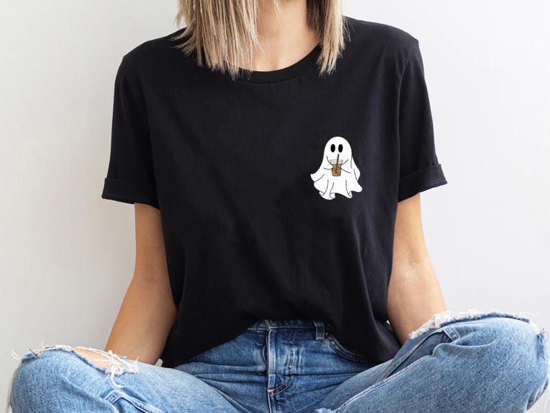 Pu&ograve; includere: Una maglietta nera con un fantasma bianco che tiene una tazza di caff&egrave;. Il fantasma ha due occhi e un piccolo sorriso.