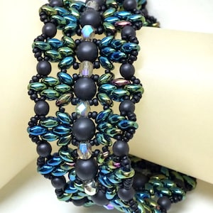 May include: A beaded bracelet featuring black, green, and iridescent blue beads. The bracelet is crafted with a range of bead shapes and sizes, resulting in a distinctive and elaborate design.